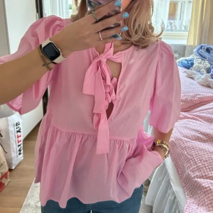 Rosa blus med knyt och puffärm - Söt rosa blus med två knyt framtill och puffiga korta ärmar. Blusen har en lös passform och volang nedtill. Bara hängt i garderoben så den är aldrig använd🩷
