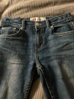 Levis jeans, slimfit - Säljer ett par klassiska blå jeans från Levi's med raka ben och femficksmodell. Jeansen har tydliga sömmar på bakfickorna och en liten röd Levi's-tag. Materialet är slitstarkt denim i bomull. Perfekta för en avslappnad och tidlös stil.