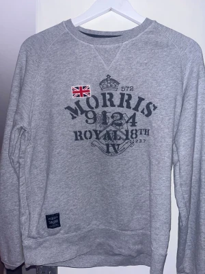 Grå sweatshirt från Morris - Snygg grå sweatshirt från Morris med tryck framtill och en liten brittisk flagga på bröstet. Tröjan har rund halsringning och långa ärmar. Perfekt för en avslappnad och stilren look.