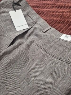 These Glory Days T Noble Pow Check rutiga byxor, storlek 58 - Snygga kostymbyxor från These Glory Days i grått med diskret rutmönster. Klassisk rak passform, bälteshällor och bakficka med passpoal. Perfekta för en stilren look och passar till skjorta eller t-shirt.