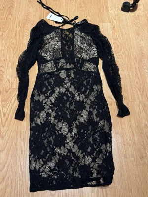 Svart spetsklänning med öppen rygg - Supersnygg svart spetsklänning från bikbok med långärmade spetsärmar och öppen rygg. Knytband i nacken och figurnära passform. 