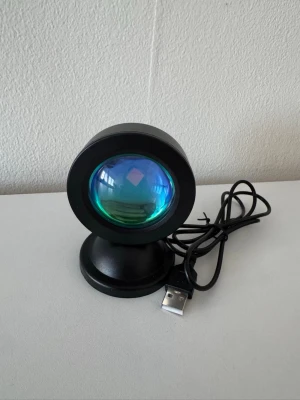 Flerfärgad USB solnedgångslampa svart - Cool solnedgångslampa med USB-anslutning. Lampan har ett svart runt hölje och projicerar ett varmt orange ljus som skapar en snygg solnedgångseffekt på väggen. Perfekt för att skapa mysig stämning i rummet eller till kreativa foton.