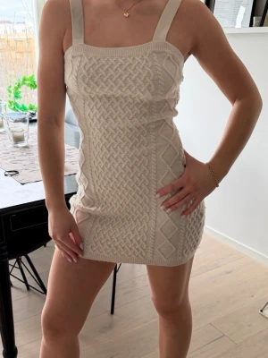 Beige stickad kort klänning H&M - Superfin beige stickad klänning från H&M i kort modell. Klänningen har breda axelband, fyrkantig ringning och ett snyggt kabelstickat mönster framtill. Perfekt för dig som gillar en trendig och bekväm look🥰✨