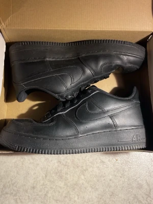 Nike Air Force 1 Low helsvart - Klassiska Nike Air Force 1 Low i helsvart läder. Skorna blev försmå efter nån månad. Skorna är i bra skick. Skorna är kostade 1 399kr på kidsbrandstore.se om någon undrar