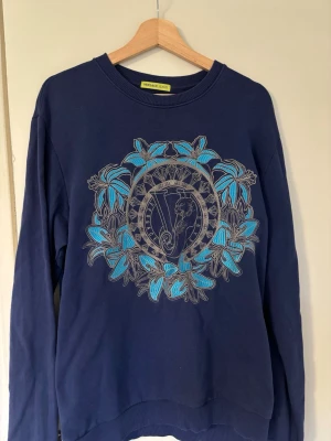 Blå sweatshirt från Versace Jeans - Väldigt unik sweatshirt från versace jeans. Ända defekten är som visas på bild 4 men det är ingenting man ser om man ej kollar jättenoga. Nypris 3000+