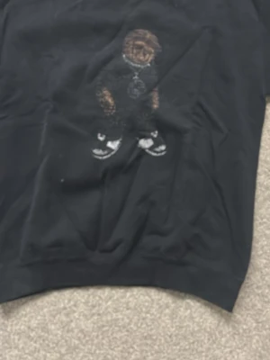 Svart tröja med björnmotiv - Cool svart tröja med ett broderat björnmotiv på bröstet. Tröjan har rund hals och är i en klassisk passform. Perfekt för dig som gillar streetwear och vill ha något unikt i garderoben.