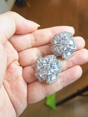 Glittriga blomformade örhängen - Säljer ett par riktigt glittriga örhängen i silverfärg med stor blomformad design. Örhängena är täckta av gnistrande stenar i olika former och storlekar som ger en lyxig och iögonfallande look. Perfekta för dig som vill sticka ut och älskar statement-smycken.