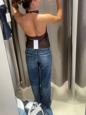 Blå raka jeans med låg midja - Säljer ett par klassiska blå jeans med rak passform och låg midja. Jeansen har fem fickor, silverfärgade nitar och knapp, samt subtila slitningar för en avslappnad look. Perfekta till vardagsstilen och tillverkade i denim av bomull.