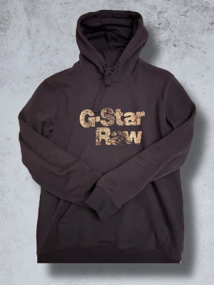 Svart hoodie från G-Star  - Säljer en svart hoodie från G-Star Raw med stor guldfärgad logga på bröstet. Nästan aldrig använt då jag anser tröjan varit lite för stor för mig, men är kort…😅Priset är inte skrivet på sten, bara att hojta til!