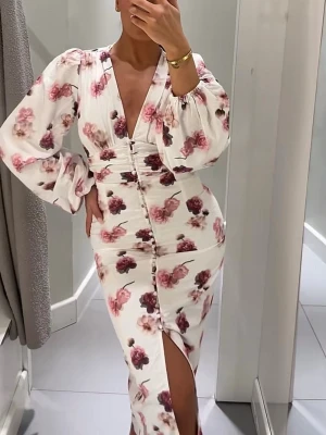 Viral blommig långklänning med slits - Supersnygg långklänning med blommigt mönster i rosa och vinröda toner på vit botten. Djup v-ringning, långa puffärmar och knappar framtill. Klänningen har en slits framtill och markerad midja för en feminin siluett. Perfekt för sommarens alla tillfällen. Viral och slutsåld!