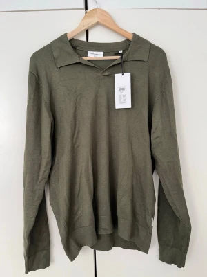 Olivgrön tröja från Lindbergh - Snygg olivgrön långärmad tröja från Lindbergh i slim fit-modell. Tröjan har en klassisk krage och är tillverkad i ett mjukt, tunt material som passar perfekt till lager på lager. Enkel och stilren design som funkar till det mesta. Varan har ej används då den har prislappen kvar från köpet av varan. Tyvärr har den en färgmissbildning baktill runt kragen. Den är ändå väldigt snygg. Original priset ligger på 599kr men jag säljer den för 299kr. Hör alltid av dig om du vill diskutera priset! 