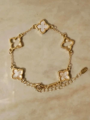 Guldfärgat armband med vita clover-detaljer✨ - Snyggt armband i guldfärg med fem fyrklöverformade länkar fyllda med vit pärlemor. Kedjan är tunn och har justerbar längd med karbinlås✨