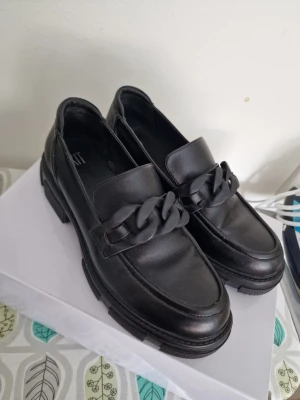 Svarta chunky loafers från XIT - OBS Jag kan fixa fri frakt, kontakta mig innan köp. Säljer ett par svarta chunky loafers från XIT med bred sula och en cool kedjedetalj över foten. Skorna är i skinnimitation och har en stilren, modern look som passar till många outfits. Storlek 41, knappt använda. 