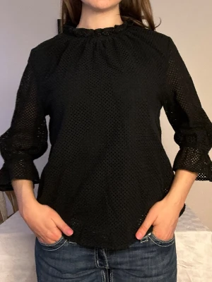 Svart  hålmönstrad Carin Wester blus🖤 - Snygg svart blus med hålmönstrad struktur och volang vid halsen. Blusen har trekvartsärm med lätt utsvängda ärmslut och är tillverkad i ett tunt, luftigt material. Perfekt att styla med jeans eller kjol för en trendig look.🖤