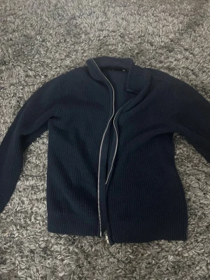 Mörkblå stickad kofta med dragkedja - Mysig mörkblå stickad kofta från 157 med dragkedja framtill. Koftan har ribbstickad struktur, hög krage och långa ärmar. Perfekt för lager på lager och enkel att matcha med olika outfits.