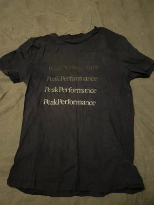 Mörkblå Peak Performance t-shirt - Snygg mörkblå t-shirt från Peak Performance med tryck i flera olika nyanser av loggan på framsidan. Klassisk rund hals och korta ärmar. Perfekt till jeans eller shorts för en avslappnad look.