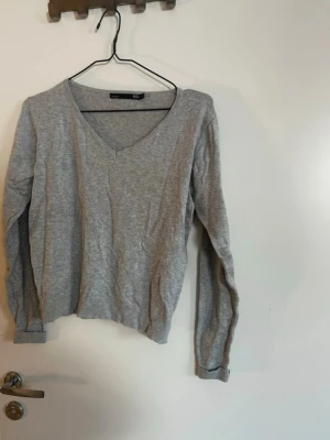 Grå V-ringad tröja från Lager157 - En enkel och stilren grå tröja från Lager157 med V-ringning och långa ärmar. Tröjan har ribbade muddar vid ärmslut och nederkant, perfekt för lager på lager. Tillverkad i mjukt och tunt material som känns skönt mot huden. Rök och djurfritt hem. Pruta gärna !🌸