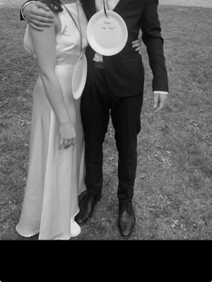 Ljusrosa långklänning i satin - Elegant ljusrosa långklänning i glansigt satinmaterial med hög halsringning och ärmlös design. Klänningen har en rak, flytande siluett och passar perfekt till speciella tillfällen. Enkel men stilren look som ger en lyxig känsla.