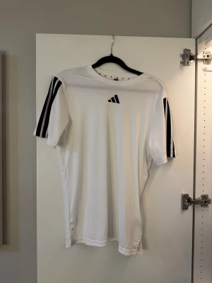 Vit träningströja med svarta detaljer - Snygg vit träningströja från Adidas med klassiska svarta ränder på axlarna och Adidas-logga på bröstet. Perfekt till träning!☺️🩵 aldrig använd