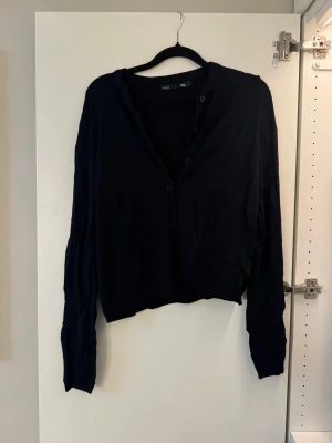 Svart kofta från Lager 157 - En svart, tunn kofta från Lager 157 med knappar framtill. Enkel och stilren design, perfekt att slänga över en topp. Storlek L men känns som XS/S!!💛