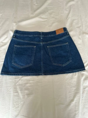 Mörkblå jeanskjol med fickor - Snygg mörkblå jeanskjol i klassisk modell med fem fickor och bälteshällor. Kjolen har en rak passform och är sydd i kraftigt denimtyg med kontrastsömmar. Perfekt att matcha med en enkel topp eller hoodie.