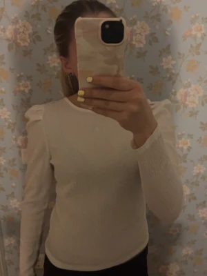 Vit långärmad blus med knyt - Stilren vit blus i ett lätt, krinklat tyg med lång ärm och puff vid axlarna. Blusen har en rundad ringning med dekorativ knytning bak som ger en trendig touch. Har en svag sminkfläck men inget man tänker på. Använd ett fåtal gånger🫶🏼🫶🏼