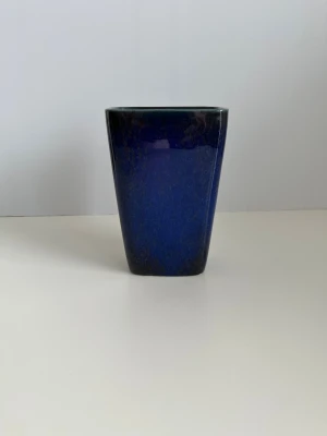 Blå vas i högblank keramik  - Superfin blå keramikvas med en färgspräcklig högblank glasyr / yta. Vasen har en rektangulär form som smalnar av mot botten. Den är lämplig för att visa blommor eller som en dekorativ inredningsdetalj. Ca 17 x 11 x 7 cm. Mycket fint skick, som ny!