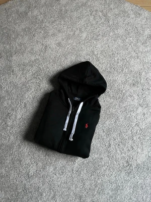 Polo ralph lauren zip-up hoodie - Säljer min Ralph lauren zip-up då den inte passar mig. Den är bara använd en gång. Det är en stilig och bekväm hoodie i färgen svart och passar i alla tillfällen. Hör av er om ni vill ha fler bilder eller har frågor!