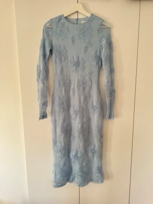 Ljusblå klänning - Superfin ljusblå långklänning med spetsdetaljer. Klänningen har en kroppsnära passform och transparent mesh med broderade blommor över hela plagget. Endast använd vid ett tillfälle. 