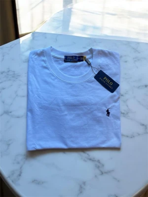 Vit t-shirt från Polo Ralph Lauren - Klassisk vit t-shirt från Polo Ralph Lauren med rund halsringning och den ikoniska lilla broderade loggan på bröstet. Tillverkad i mjuk bomull och har en enkel, stilren design som passar till allt.