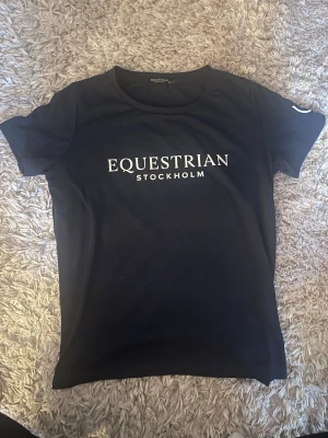 Svart t-shirt från Equestrian Stockholm - Snygg t-shirt från Equestrian Stockholm med vit logga framtill. Klassisk rund halsringning och korta ärmar. Perfekt för dig som gillar stilrena plagg med sportig känsla. Materialet känns mjukt och följsamt. Helt oanvänd inte ens provad säljer då jag slutat rida💓