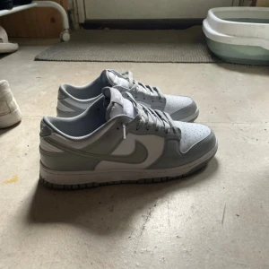 Nike Dunk Low grå/vita sneakers - Nike dunk low, white/light smoke grey i storlek 43. Dom är unisex och använda i mindre än en vecka. Säljes pågrund av att dom var för små för mig. Pris kan diskuteras