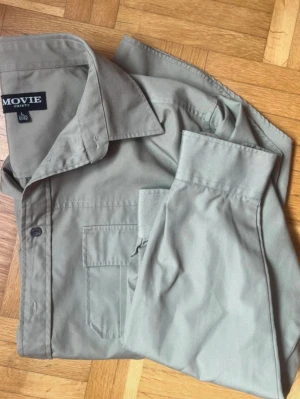 Beige vintege skjorta från Movie Shirts - Stilren beige skjorta från Movie Shirts med klassisk krage, bröstficka och knappar framtill 🌻 Skjortan är hämtat direkt från morfars garderob, då han använde den mycket för kanske 40-50 år sedan 🪩 Den har långa ärmar och är tillverkad i mjuk bomull, perfekt för en clean och enkel look 🌷Priset går att diskutera 💕