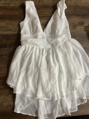 Vit omlottklänning med volanger - Snygg vit kortklänning med omlott och volangdetaljer. Djup v-ringning och ärmlös. Perfekt för sommaren och student. Luftigt skönt material