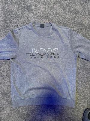 Grå Hugo Boss sweatshirt – Storlek M – Stilren - Snygg och bekväm sweatshirt från Hugo Boss i en snygg melerad grå nyans. Modern logga över bröstet som ger en lyxig känsla. Passar lika bra till jeans som till mer dressade byxor. • Märke: Hugo Boss • Storlek: M • Skick: Fint skick • Passform: Normal i storleken Säljes då den tyvärr inte kommer till användning. Skickas inom 24 timmar! 