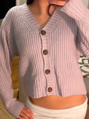 Ljuslila stickad kofta med knappar🌸 - Säljer en ljuslila stickad kofta med grov ribbstickning och stora bruna knappar framtill. Koftan har v-ringning, långa ärmar och en croppad passform. 