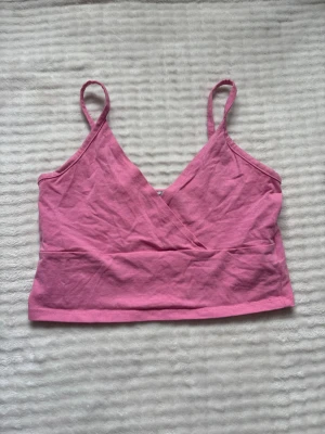 Rosa omlott linnetopp - Söt rosa linnetopp med omlottdesign och smala axelband. Toppen är croppad och har en djup v-ringning både fram och bak. Perfekt för varma dagar och enkel att matcha med jeans eller kjol.