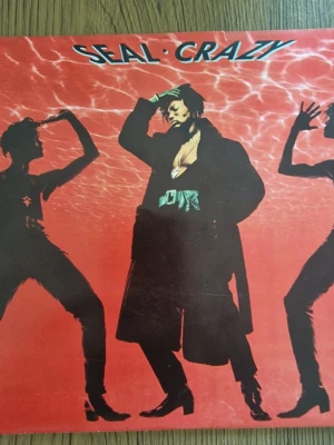 Seal Crazy vinylsingel - Vinylsingel med Seal, låten 'Crazy'. Omslaget är rött med silhuetter av personer och Seal i mitten. Texten 'Seal Crazy' står högst upp. Producerad av Trevor Horn och utgiven av ZTT Records. Baksidan är röd med låttitlar och streckkod.