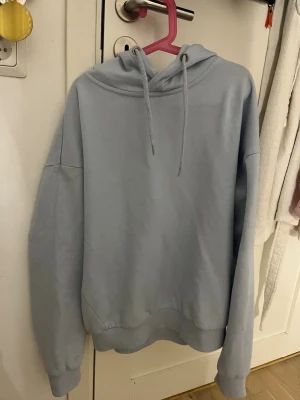Ljusblå oversized hoodie - Säljer en ljusblå hoodie med oversized passform och klassisk huva med dragsnören. Hoodien har ribbade muddar vid ärmslut och nederkant. Perfekt för en chill och avslappnad stil.