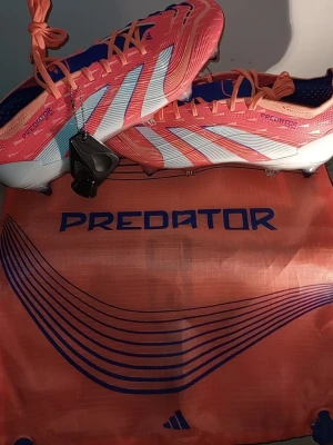 Adidas Predator elite fotbollsskor orange HELT NYA!!! - HELT NYA FOTBOLLSSKOR .Snygga Adidas Predator fotbollsskor elite i orange med vita och blå detaljer. Skorna har en modern, strömlinjeformad design med snörning och mönstrad ovandel för extra grepp på planen. Tillverkade i syntetmaterial och levereras med matchande påse+extra metal dobbar.