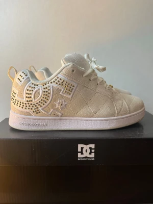 DC sneakers 💖 - Snygga vita sneakers från DC Shoes med quiltad ovandel och guldfärgade detaljer på snörningen. Skorna har en låg siluett och dekoreras med guldfärgade nitar på sidan som formar DC-loggan. Perfekta för dig som vill sticka ut med stilrena detaljer, endast använda två gånger🌸