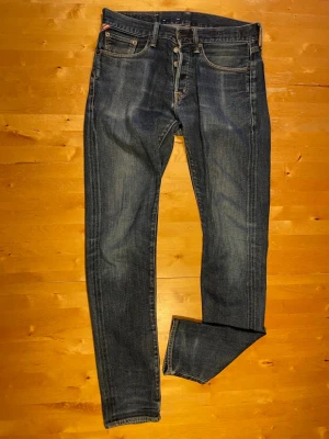 Levi's 511 Slim Fit blå jeans - Säljer ett par klassiska Levi's 511 Slim Fit jeans i mörkblå denim med snygga slitningar och femficksmodell. Jeansen har knappgylf och bruna kontrastsömmar. Perfekta för dig som gillar en smalare passform och tidlös stil.