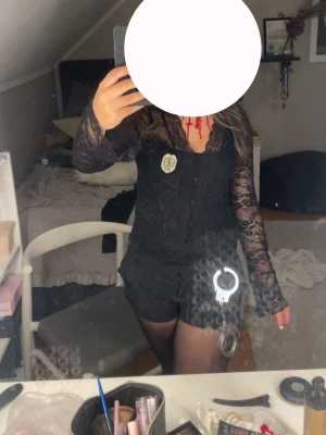 Svart spetsblus - Svart långärmad blus i spets med knappar framtill och djup v-ringning. Blusen har transparenta ärmar och figurnära passform. Använd en två gånger.