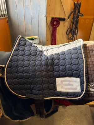 Mörkblått schabrak med vit kant - Kan gå ner i pris vid snabb affär. Säljer ett mörkblått schabrak från Equiline, e-logga med vit kant. Fint skick men använd. Strl full. Tvättas såklart innan de postas☺️