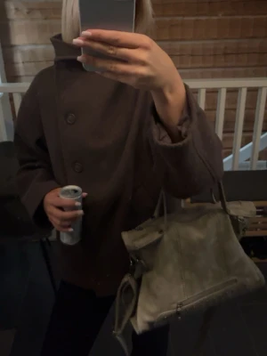 Brun ullkappa med bred krage - Kort brun kappa i ullmix med oversized passform och bred krage. Kappan har stora knappar framtill och vida ärmar för en avslappnad look. Perfekt för dig som gillar minimalistisk och trendig stil.