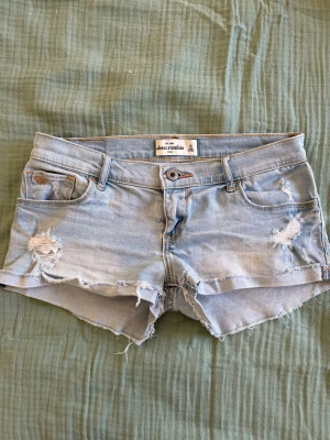 Ljusblå jeansshorts Abercrombie - Säljer ett par ljusblå jeansshorts från Abercrombie med slitna detaljer och fransig kant. Är i storlek kids 16 men skulle säga att de passar som en xs.