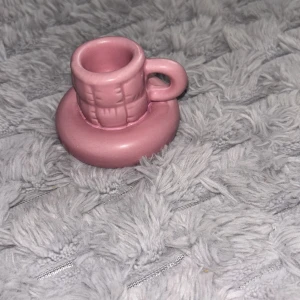 Liten rosa ljushållare i keramik - Söt liten ljushållare  fat i rosa keramik. Koppen har ett handtag och ett diskret rutmönster på utsidan. Perfekt som dekoration eller till dockservis. Rund form och blank yta.