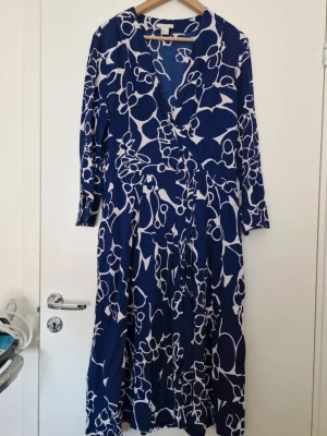 H&M blåvit omlottklänning med blommönster - Snygg långklänning i blått och vitt med blommigt mönster och omlottmodell. Klänningen har v-ringning och trekvartsärm, perfekt för sommarens alla tillfällen. Luftigt material och skön passform. Storlek 40. 100% viskos. Perfekt skick