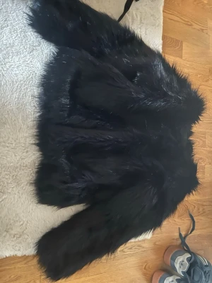 Svart fluffig pälsjacka - Säljer en svart, superfluffig pälsjacka med lång lugg och breda ärmar. Jackan har en klassisk, rak passform och ger en riktigt lyxig känsla. Perfekt för dig som vill sticka ut och hålla dig varm under kalla dagar.
