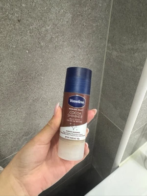 Vaseline Cocoa Shimmer Jelly Stick - Vaseline Cocoa Shimmer Jelly Stick är en återfuktande kroppsgelé i stiftform med skimrande effekt. Produkten har en brun och blå förpackning och innehåller kakaodoft. Perfekt för att ge huden extra glow och lyster.  ANVÄND EN GÅNG!!!